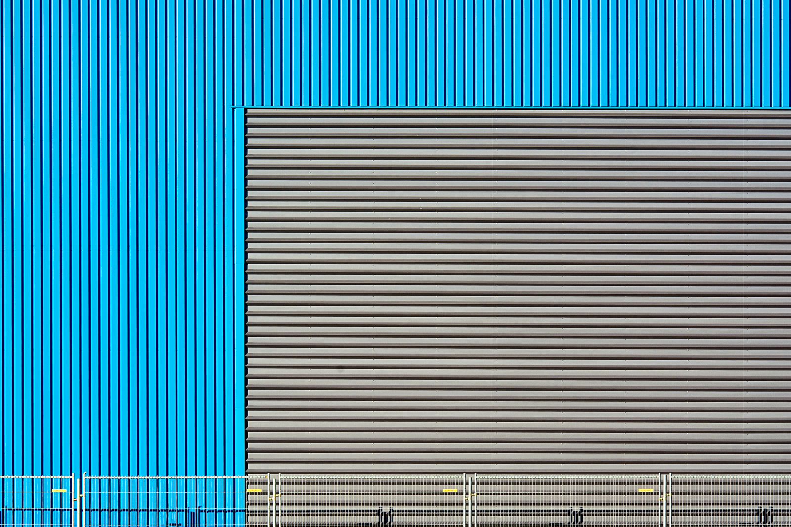 Close-up of an industrial building facade with blue and grey corrugated metal patterns.