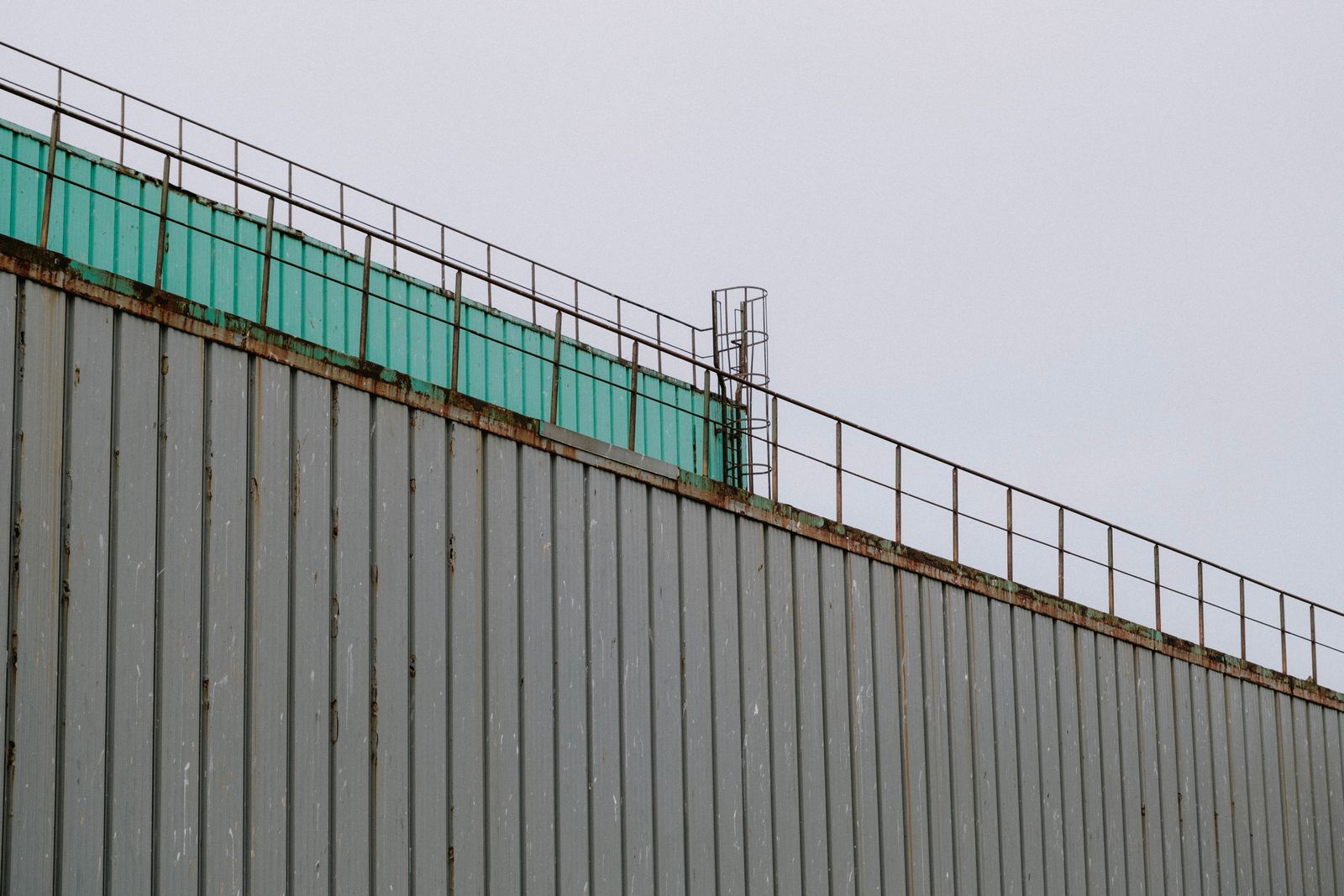 Close-up of a rusty industrial roof with a green railing against a clear sky.