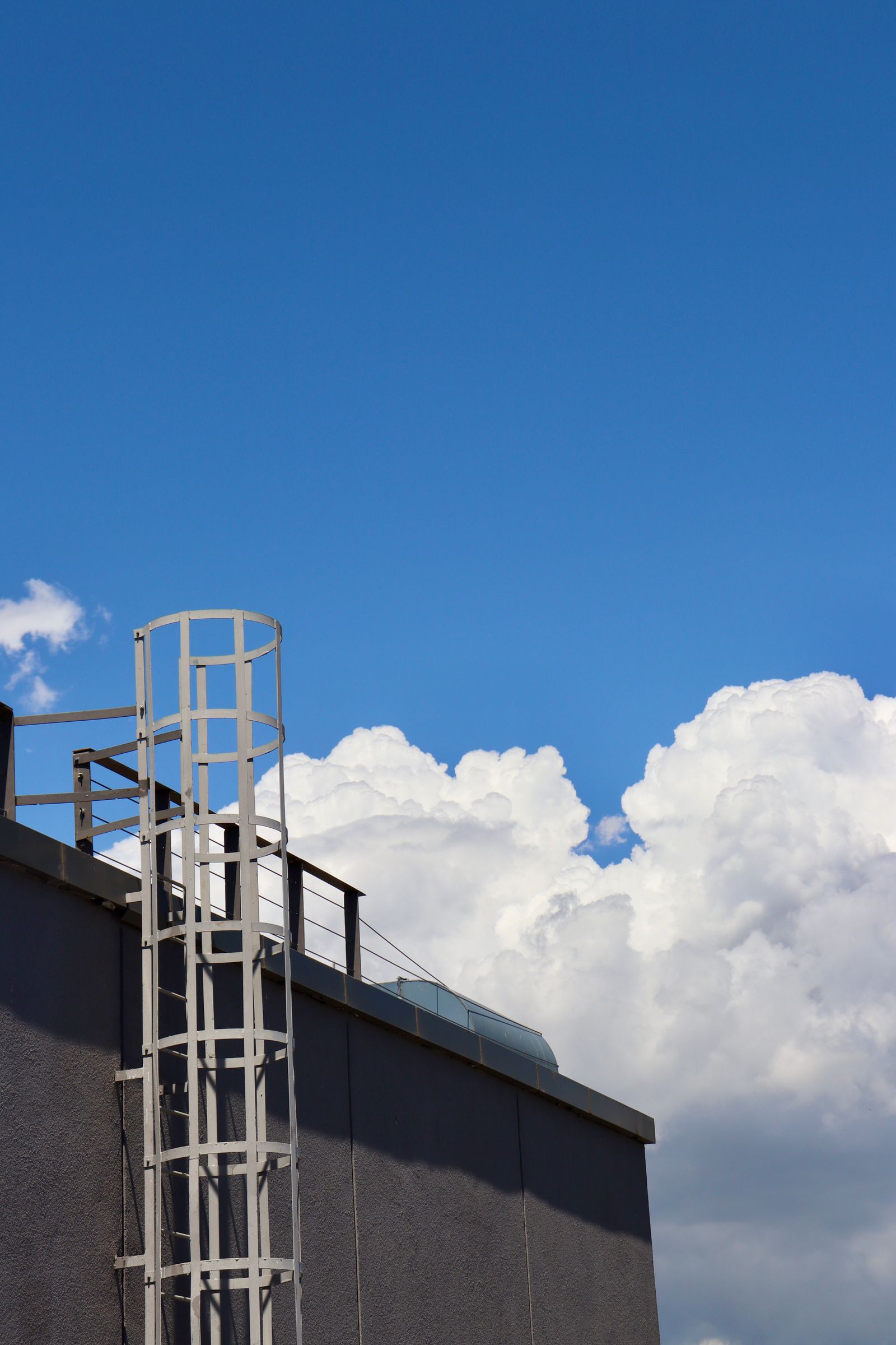A rooftop of an industrial building under a bright blue sky with fluffy clouds.